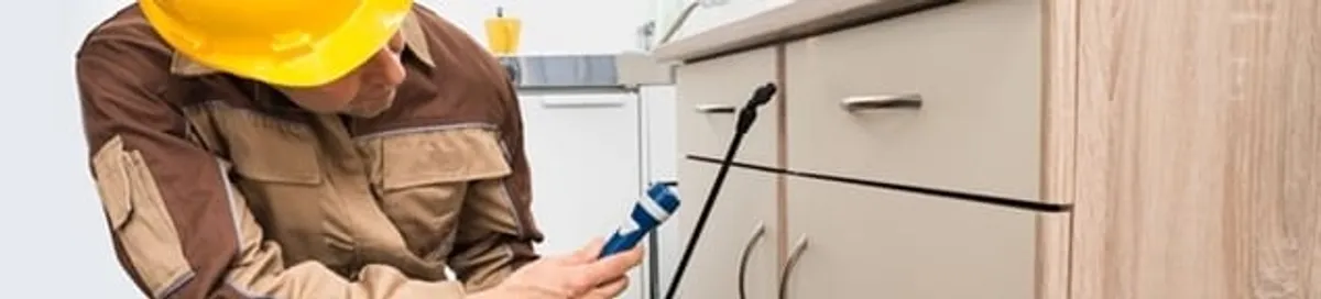 Roach exterminator applying treatment under kitchen cabinets in San Jose, CA