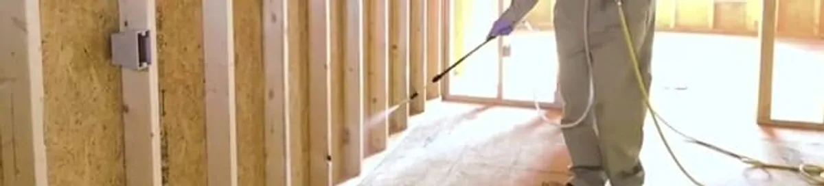 Termite treatment technician applying spray along framing and unfinished walls in San Jose, CA
